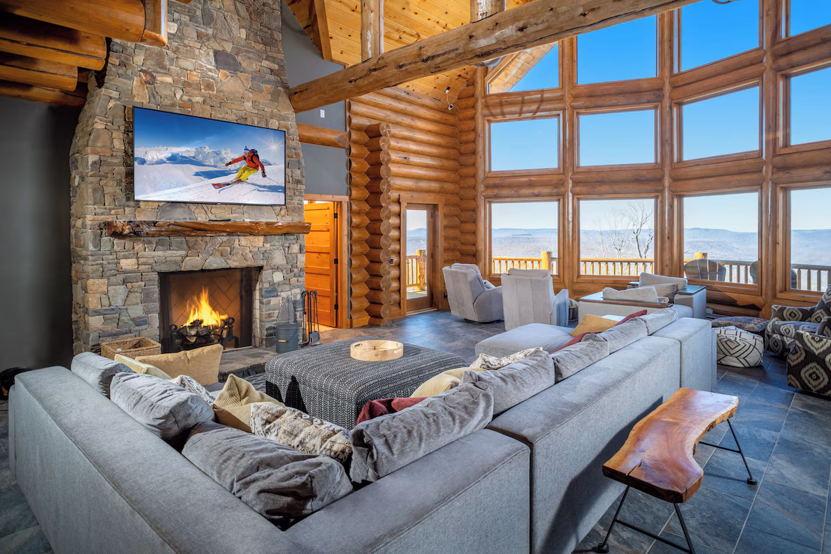 Great room with tall glazing, stone fireplace, seating and mountain outlook